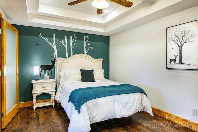 bedroom with dark hardwood / wood-style floors, ceiling fan, and a tray ceiling