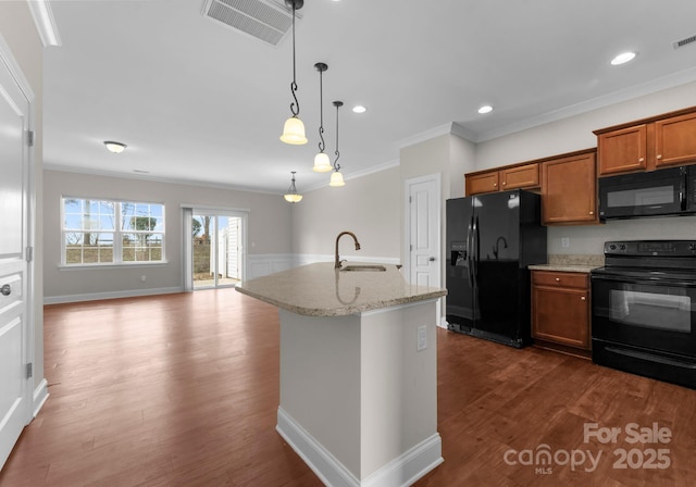 kitchen featuring sink, light stone countertops, ornamental molding, an island with sink, and black appliances