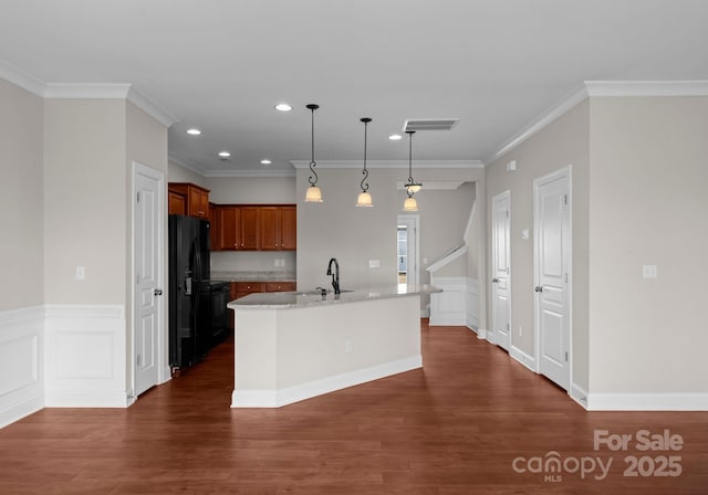 kitchen with decorative light fixtures, crown molding, black fridge, and a kitchen island with sink