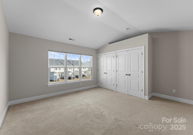 unfurnished bedroom featuring multiple closets, light colored carpet, and lofted ceiling