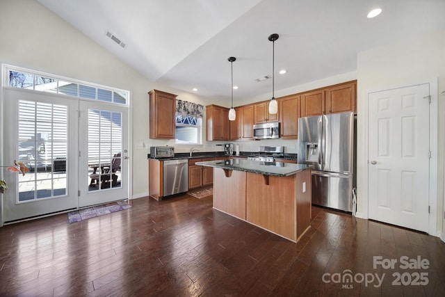 kitchen featuring dark hardwood / wood-style floors, pendant lighting, a kitchen island, appliances with stainless steel finishes, and a kitchen breakfast bar