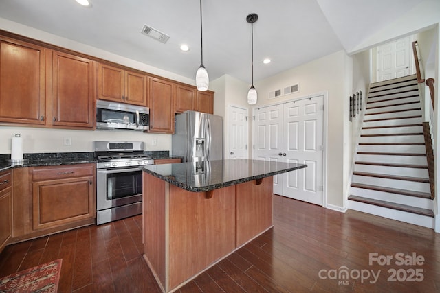 kitchen featuring stainless steel appliances, dark hardwood / wood-style flooring, dark stone counters, hanging light fixtures, and a kitchen island