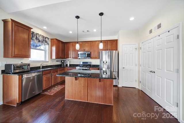 kitchen with a center island, decorative light fixtures, stainless steel appliances, dark stone counters, and sink