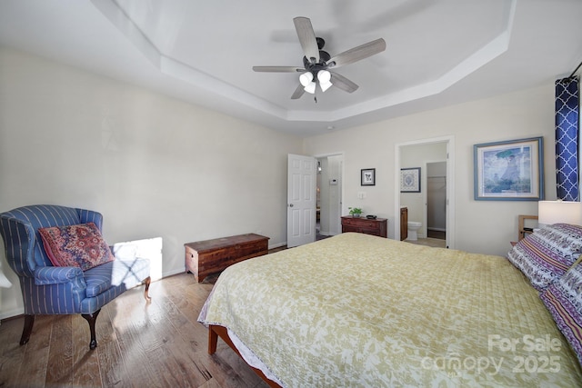 bedroom featuring a raised ceiling, ceiling fan, connected bathroom, and hardwood / wood-style floors