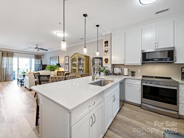 kitchen with open floor plan, a peninsula, stainless steel appliances, light countertops, and a sink