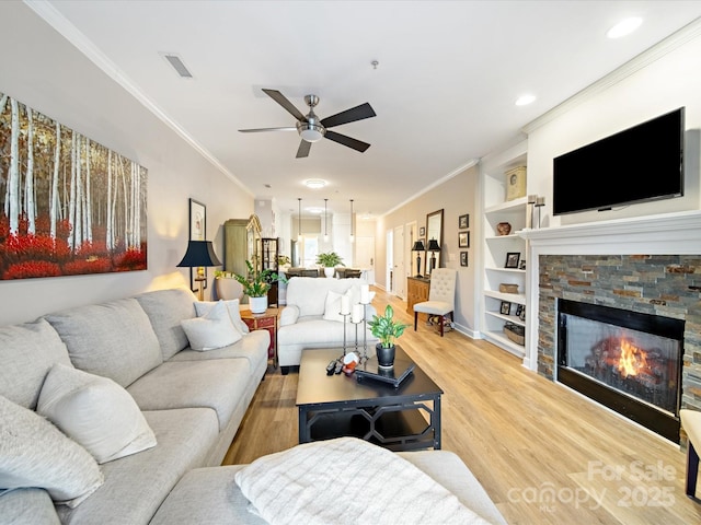 living room with visible vents, light wood-style flooring, ornamental molding, built in shelves, and a fireplace