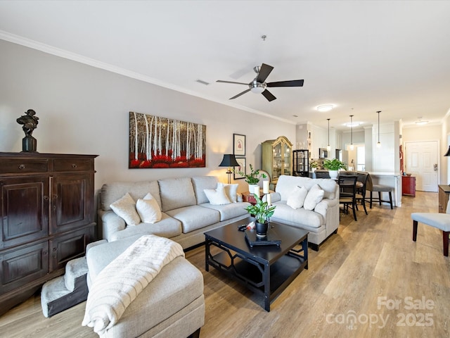 living room with light wood-style floors, visible vents, crown molding, and a ceiling fan