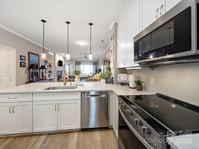 kitchen with stainless steel appliances, light countertops, open floor plan, a sink, and a peninsula