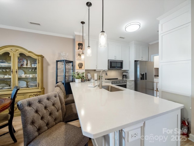 kitchen featuring appliances with stainless steel finishes, decorative light fixtures, a peninsula, light countertops, and a sink