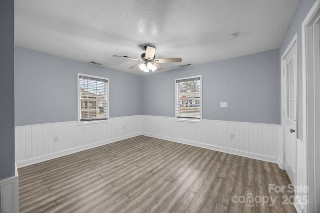 spare room with a textured ceiling, light wood-type flooring, and ceiling fan