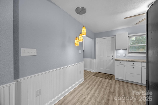 kitchen with white cabinets, a textured ceiling, light hardwood / wood-style floors, and hanging light fixtures