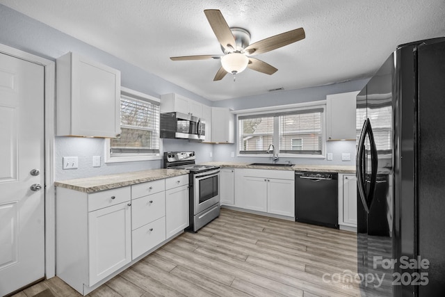 kitchen with a wealth of natural light, a textured ceiling, sink, black appliances, and white cabinetry