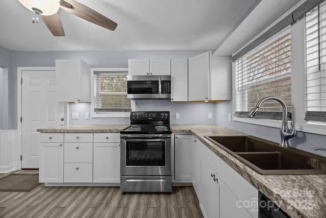 kitchen featuring white cabinetry, sink, ceiling fan, stainless steel appliances, and light wood-type flooring