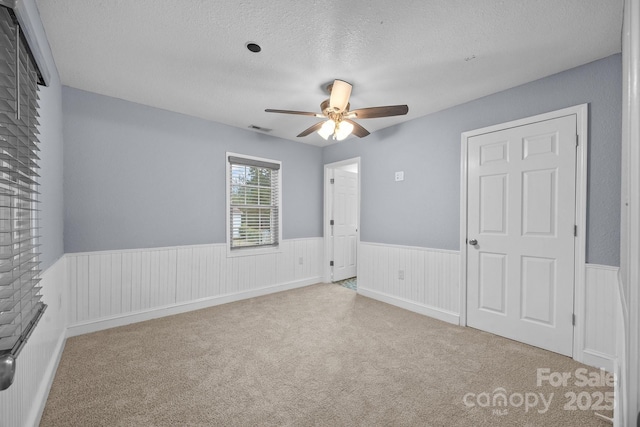 unfurnished bedroom with a textured ceiling, light colored carpet, and ceiling fan