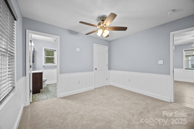 unfurnished bedroom with a textured ceiling, ceiling fan, light carpet, and ensuite bath