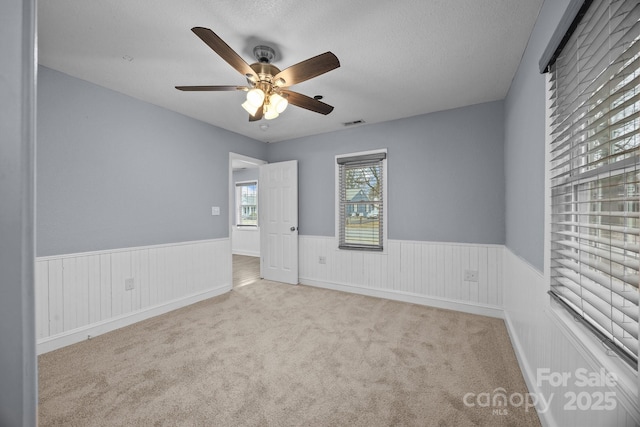 empty room with ceiling fan, light colored carpet, and a textured ceiling