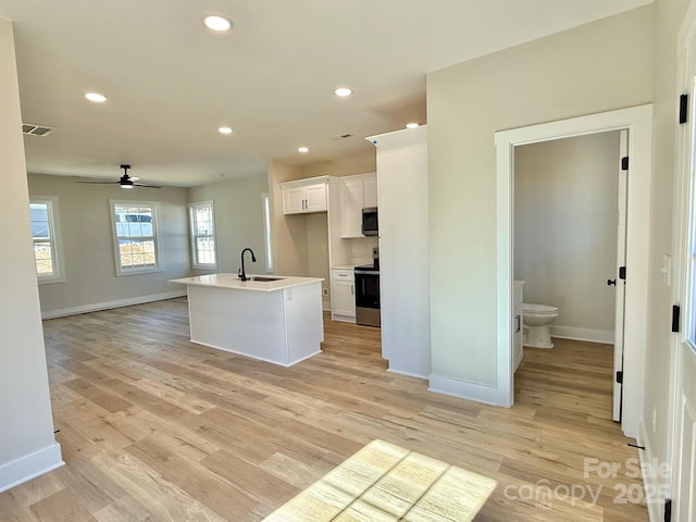 kitchen featuring sink, stainless steel appliances, an island with sink, white cabinets, and light wood-type flooring