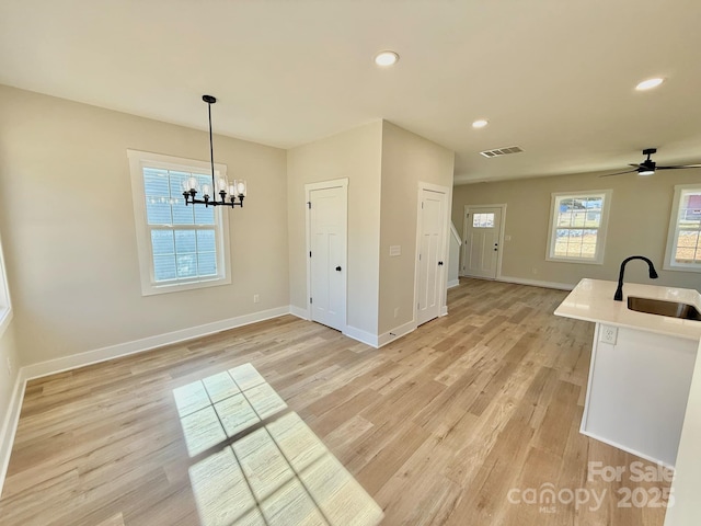 kitchen featuring light wood-type flooring, ceiling fan with notable chandelier, hanging light fixtures, and sink