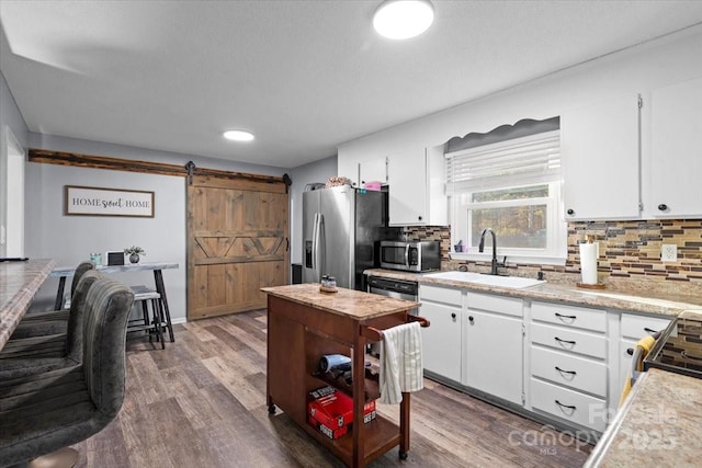 kitchen featuring sink, white cabinetry, backsplash, a barn door, and appliances with stainless steel finishes