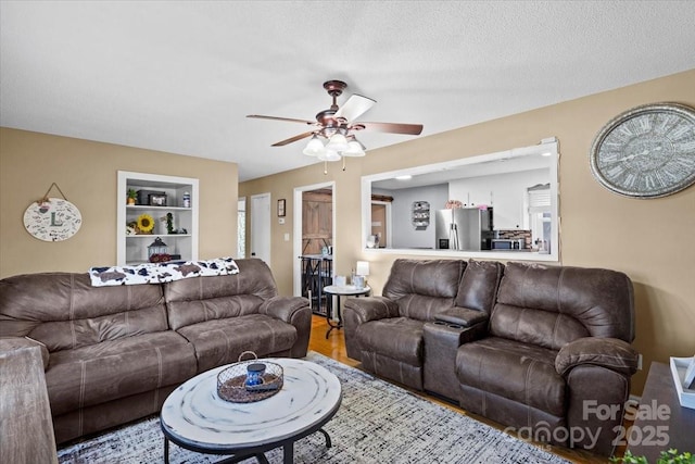 living room featuring wood-type flooring, a textured ceiling, ceiling fan, and built in shelves