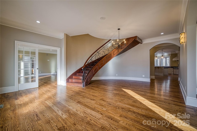 unfurnished living room with an inviting chandelier, crown molding, and wood-type flooring