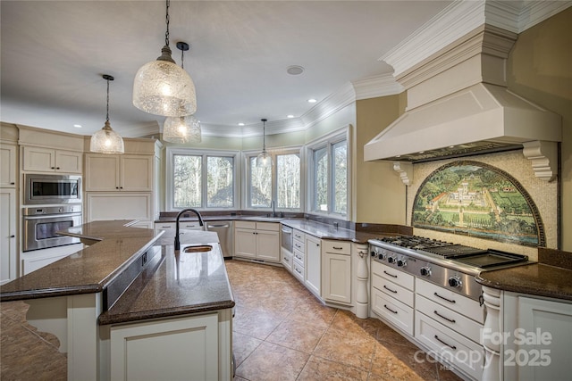 kitchen featuring custom exhaust hood, dark stone counters, hanging light fixtures, a center island with sink, and appliances with stainless steel finishes