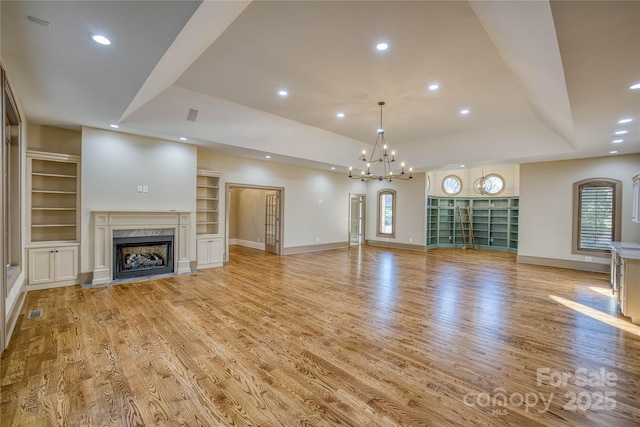 unfurnished living room with light hardwood / wood-style floors, a premium fireplace, built in shelves, and a tray ceiling