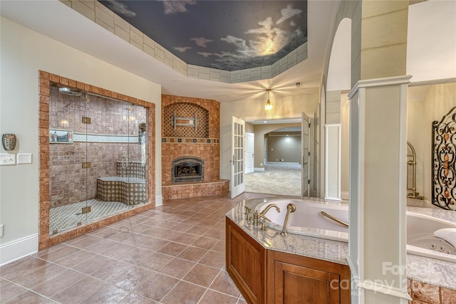 bathroom with a large fireplace, independent shower and bath, tile patterned floors, and a tray ceiling