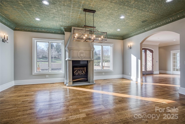 unfurnished living room with wood-type flooring, a notable chandelier, a large fireplace, and ornamental molding