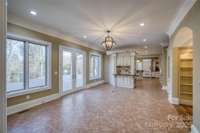 unfurnished living room with ornamental molding, french doors, and an inviting chandelier