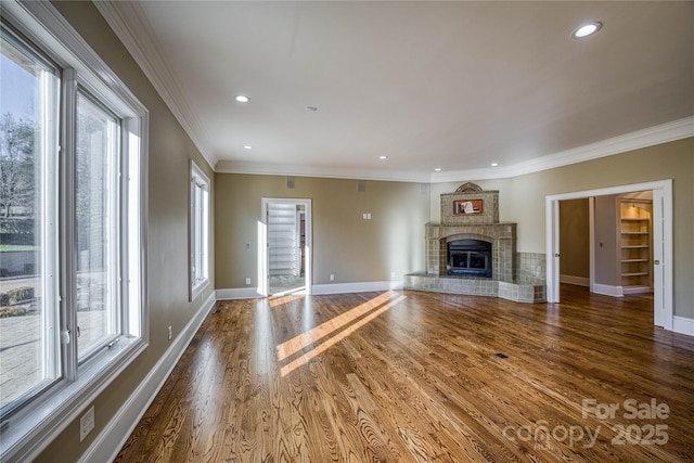 unfurnished living room featuring ornamental molding, a tile fireplace, a wealth of natural light, and dark hardwood / wood-style floors