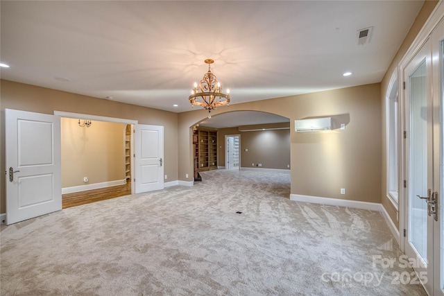 spare room featuring an AC wall unit, a chandelier, and light colored carpet