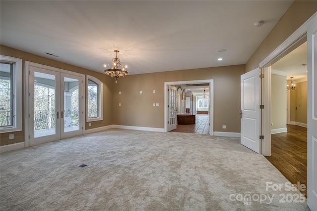 spare room with french doors, carpet flooring, and a notable chandelier