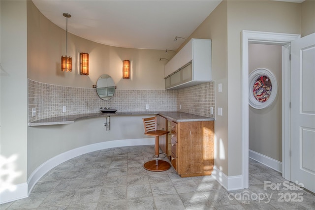 kitchen with hanging light fixtures, kitchen peninsula, light stone counters, white cabinets, and backsplash