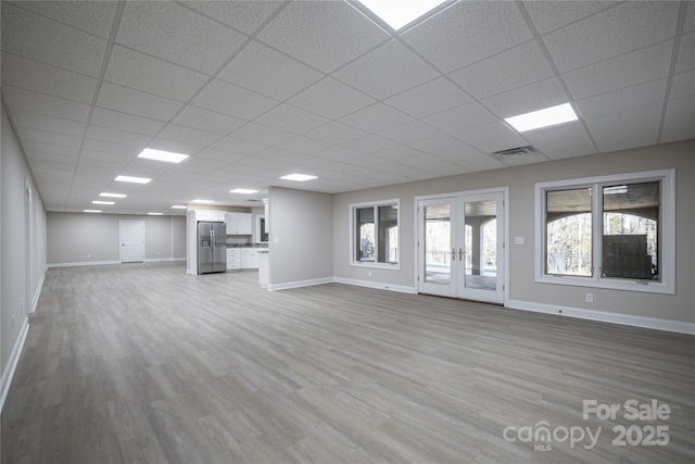 unfurnished living room featuring wood-type flooring, a drop ceiling, and french doors