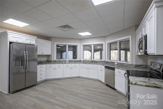 kitchen featuring white cabinetry, appliances with stainless steel finishes, a paneled ceiling, dark stone counters, and light hardwood / wood-style flooring