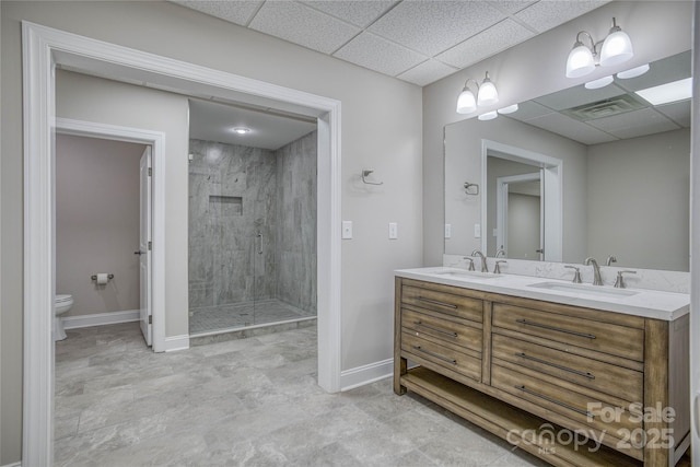 bathroom featuring a shower with door, toilet, vanity, and a drop ceiling