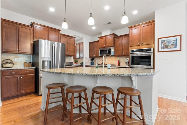 kitchen with a kitchen island with sink, a breakfast bar area, stainless steel appliances, hanging light fixtures, and sink