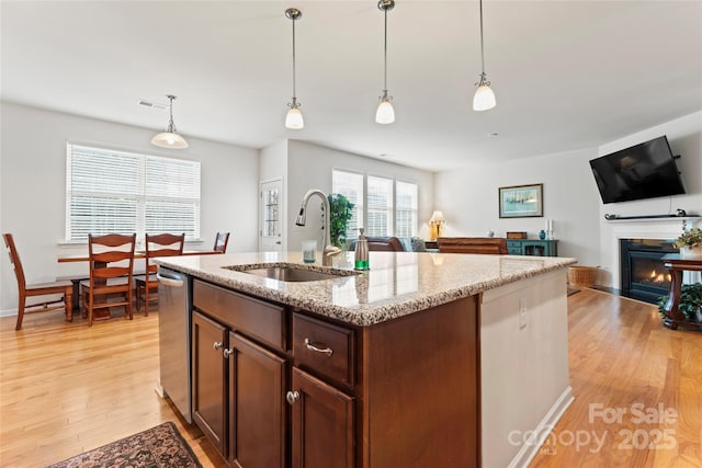 kitchen featuring sink, an island with sink, decorative light fixtures, and light stone counters