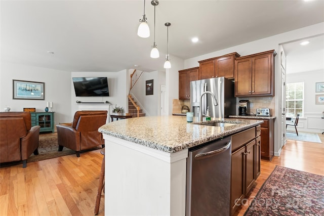 kitchen featuring light stone counters, decorative light fixtures, stainless steel appliances, a center island with sink, and sink