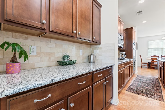 kitchen with appliances with stainless steel finishes, light hardwood / wood-style floors, tasteful backsplash, and light stone countertops