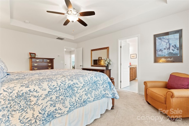 carpeted bedroom with ceiling fan, a tray ceiling, and connected bathroom