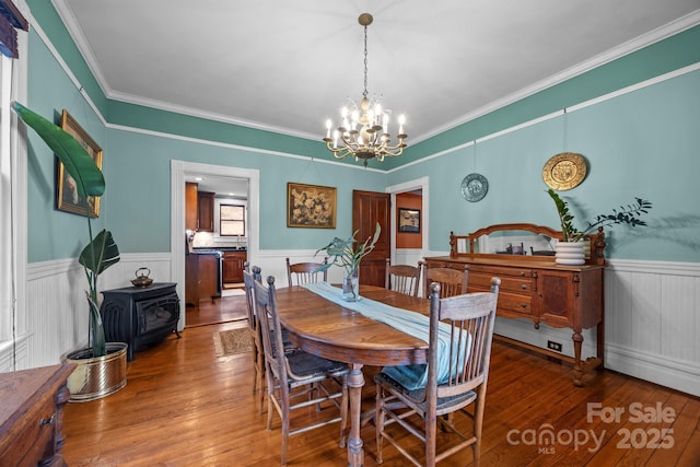 dining area featuring an inviting chandelier, hardwood / wood-style flooring, crown molding, and a wood stove