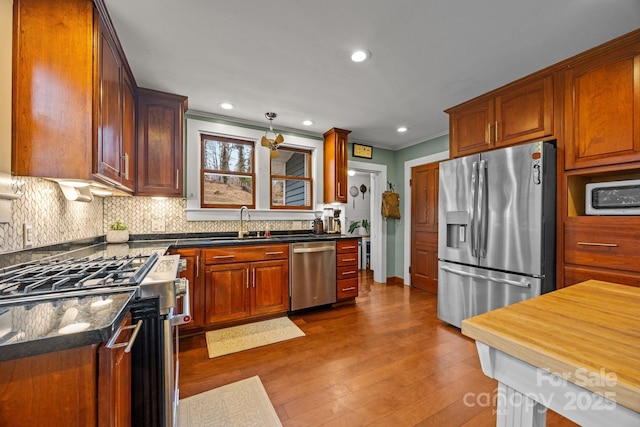 kitchen featuring sink, tasteful backsplash, wood-type flooring, ornamental molding, and stainless steel appliances