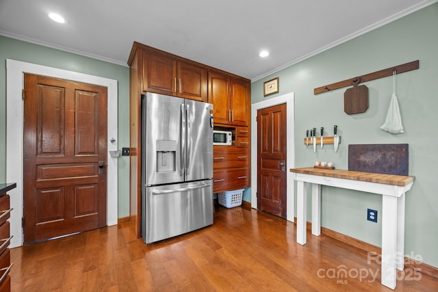 kitchen with wood counters, decorative light fixtures, wood-type flooring, crown molding, and stainless steel refrigerator with ice dispenser