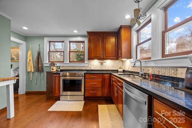 kitchen with appliances with stainless steel finishes, dark hardwood / wood-style floors, sink, dark stone countertops, and crown molding