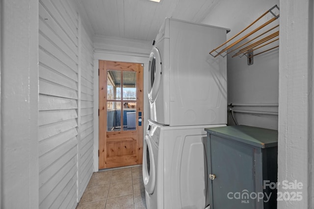 washroom with stacked washer / drying machine, light tile patterned floors, and wooden walls