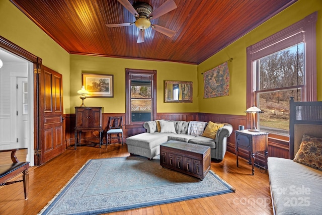 living room with wood walls, ceiling fan, crown molding, wooden ceiling, and light hardwood / wood-style flooring