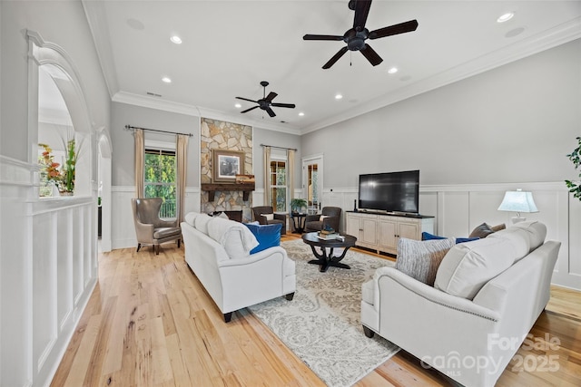 living room with ceiling fan, ornamental molding, a stone fireplace, and light hardwood / wood-style floors