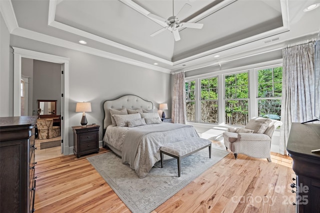 bedroom featuring ceiling fan, ornamental molding, a tray ceiling, and light wood-type flooring